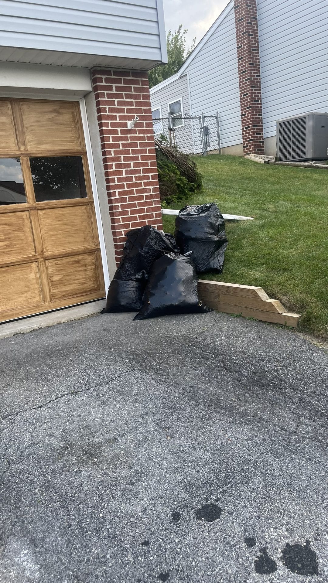 Several large black trash bags piled by a brick garage